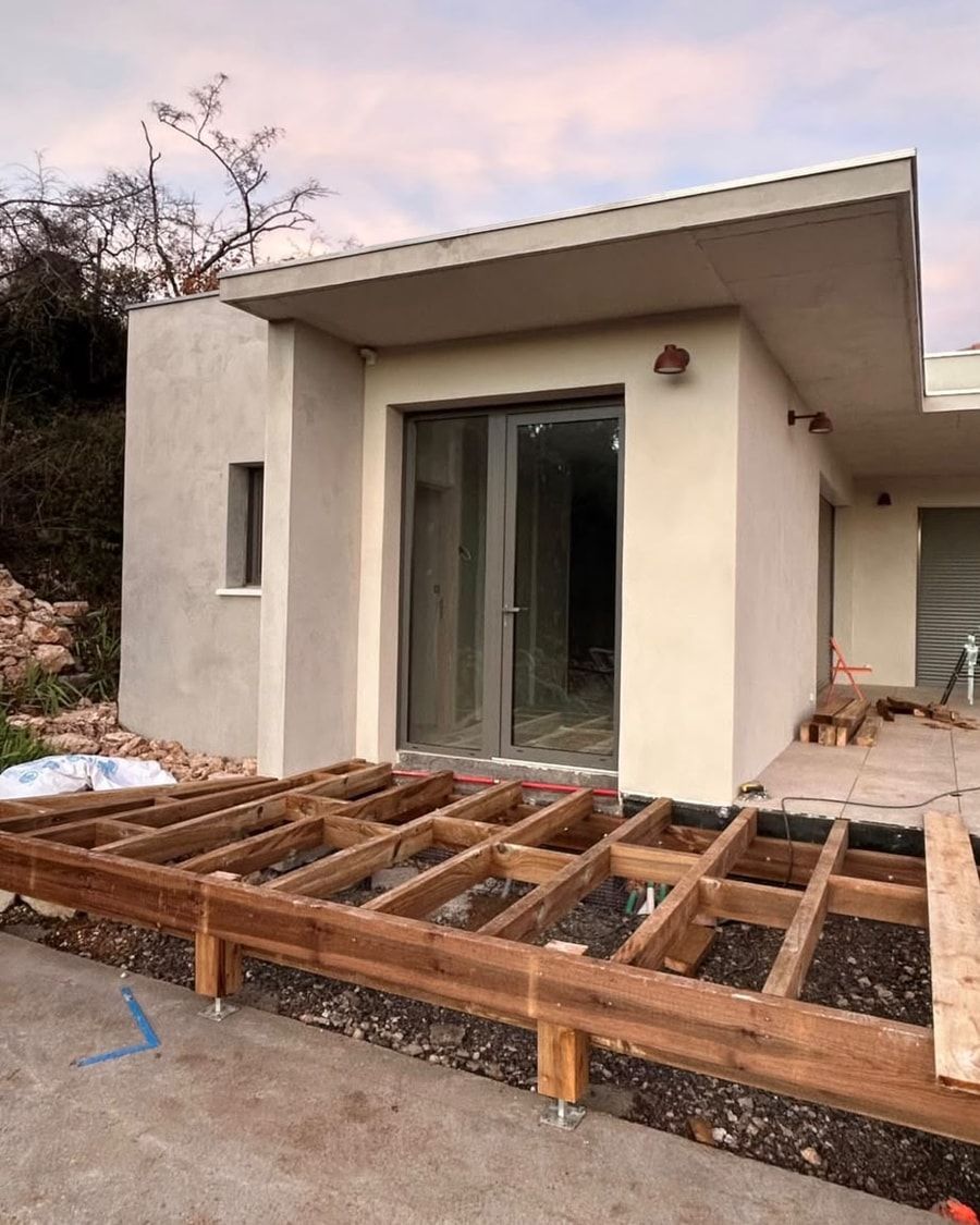 Structure de terrasse sur lambourdes et pieds réglables devant la maison, au crépuscule