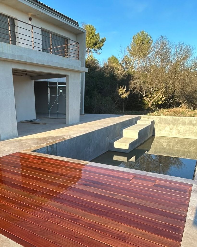 Terrasse en ipé huilé encastrée à fleur du dallage en pierre, escalier du bassin et façade enduite