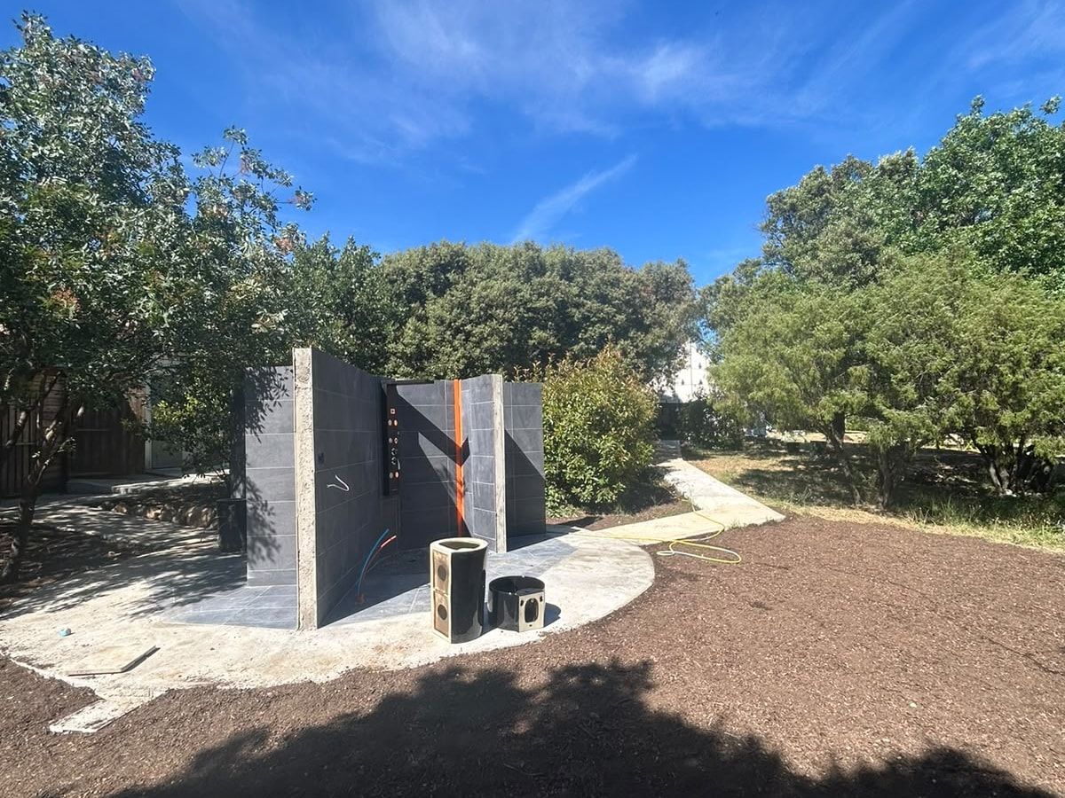 Douche extérieure en construction, carrelage anthracite sur dalle arrondie, réseaux encore apparents